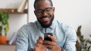 A man sitting down looking at his phone that just delivered a daily text message via a text marketing integration.