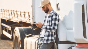 A man is leaning up against a truck texting. 