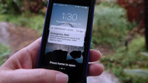 A person holding a mobile phone in their hand receiving an emergency text alert.