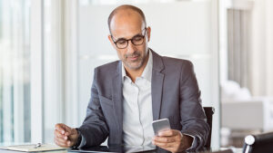A man sitting at a desk looking at his phone to determine with TextSanity tool works the best for sales texting. 