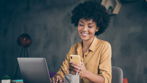 A woman sitting at a desk with a computer in front of her looking at a sales text she received. 