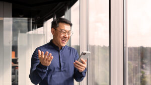 A man with a happy look on his face is looking at his mobile phone after receiving a fast sales text. 