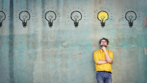 A man standing against a wall with lightbulbs drawn above his head coming up with outside the box marketing ideas.