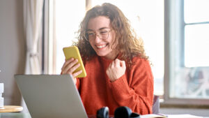 Woman excited sitting at her desk looking at the mobile phone in her hand getting an enterprise-level sms message. 